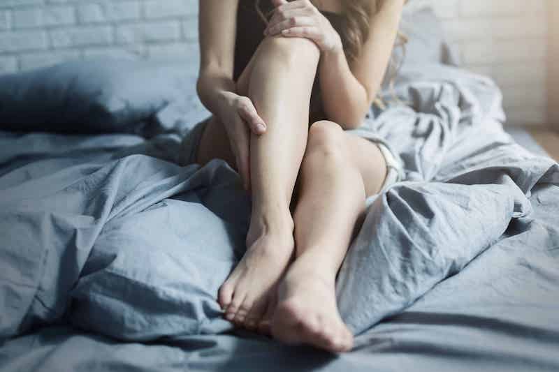 Woman sitting on bed, holding her leg